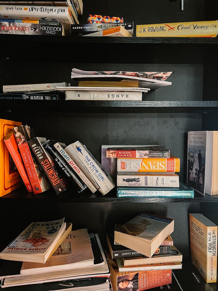 A variety of books neatly stacked on a modern black bookshelf, showcasing an eclectic collection.
